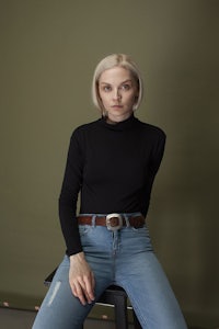 a woman in a black turtle neck top and jeans sitting on a stool