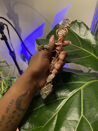 a hand holding a necklace with a large plant in the background