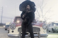 a woman wearing a black hat standing next to an old car
