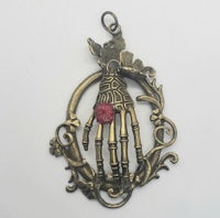 a pendant with a skeleton hand and a pink stone