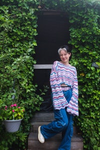a woman standing on the steps of a house wearing a striped sweater