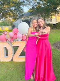 two women in pink dresses posing in front of a pink letter dz