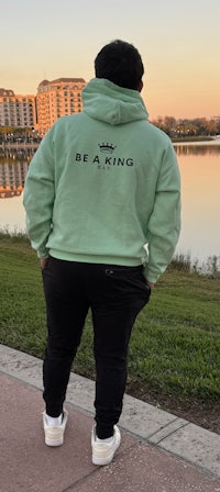 a man wearing a green hoodie with the word be king on it