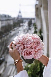 a woman holding a bouquet of pink roses in front of the eiffel tower