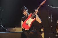a woman playing a red electric guitar on stage