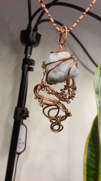a copper wire pendant hanging from a plant