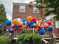a red, white and blue balloon arch in front of a house