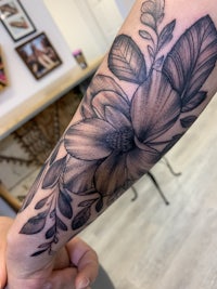 a black and grey flower tattoo on a person's forearm