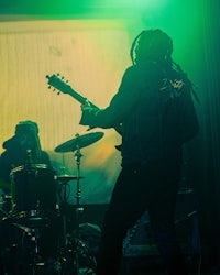 a man playing a guitar in front of a green light