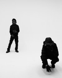 a black and white photo of two men crouching in front of a white background