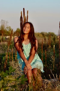 a girl in a blue dress sitting in a field of cactus