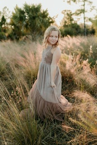 a girl in a long dress standing in tall grass