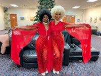 two women in red outfits posing in front of a christmas tree