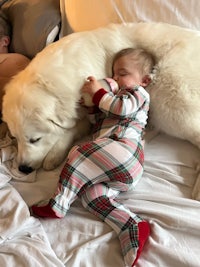 a baby in pajamas laying on top of a white dog