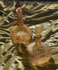 two glass decanters sitting on a golden cloth