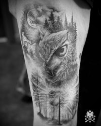 a black and white image of an owl tattoo on the thigh