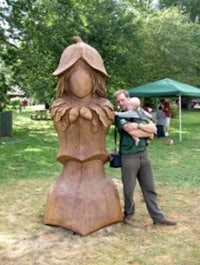 a man with a child standing next to a large wooden sculpture