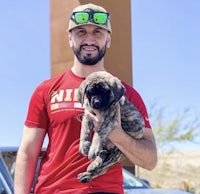 a man holding a puppy in front of a car