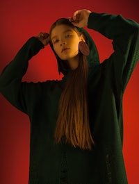a woman in a green hoodie is posing in front of a red background