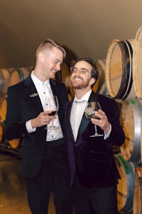 two men in tuxedos standing in front of wine barrels