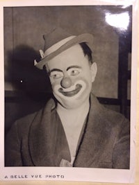 a black and white photo of a clown wearing a hat