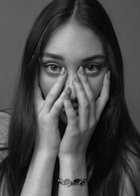 a black and white photo of a girl covering her face with her hands