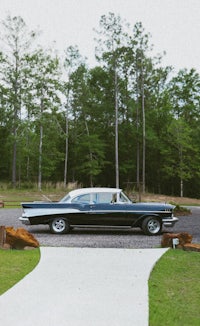 a classic car parked in front of a wooded area