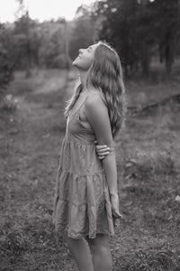 a black and white photo of a girl in a dress standing in a wooded area