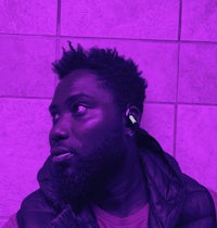 a man with a beard and earphones in front of a purple wall