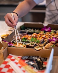 a person holding chopsticks in front of a box of food