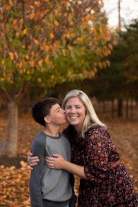 a mother and son kissing in front of a fall tree