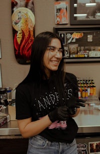 a woman smiling in front of a tattoo shop