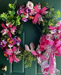 a pink wreath with flowers and bows on the front door