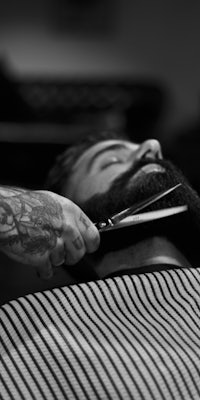 black and white photo of a barber cutting a man's beard