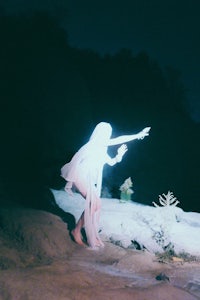a woman in a white dress standing on a rock at night