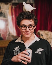 a young man holding a beer and a dove on his head