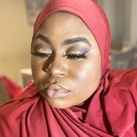a woman wearing a red hijab and gold makeup