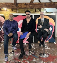 three men sitting on stools in front of a painting