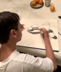 a boy is drawing on a table with oranges in front of him