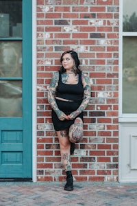 a woman with tattoos leaning against a brick wall