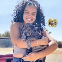 a woman holding a puppy in front of a car