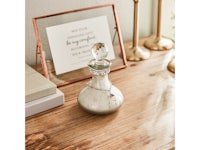 a glass decanter on a wooden table next to a frame