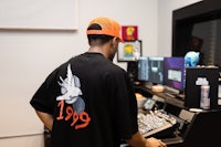 a man in a t - shirt standing in front of a mixing desk
