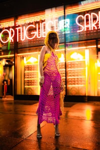 a woman wearing a crochet dress in front of a neon sign