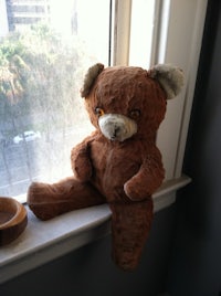 a brown teddy bear sitting on a window sill