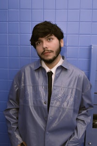a man in a blue jacket standing next to a blue wall