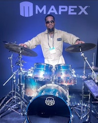 a man standing in front of a mapex drum set