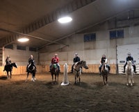 a group of people riding horses in an indoor arena