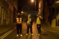 three men standing on a street at night