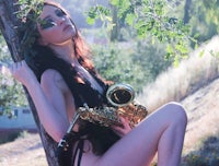 a woman sitting on a tree with a saxophone